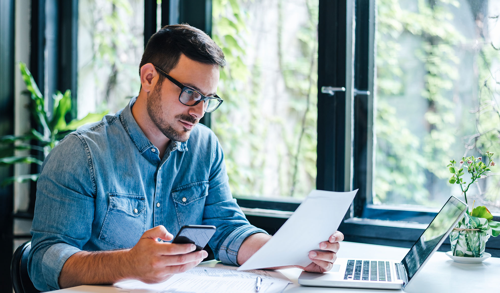 businessman-denim Serious pensive thoughtful focused young casual entrepreneur small business owner accountant bookkeeper in office looking at and working with laptop and income tax return papers and documents