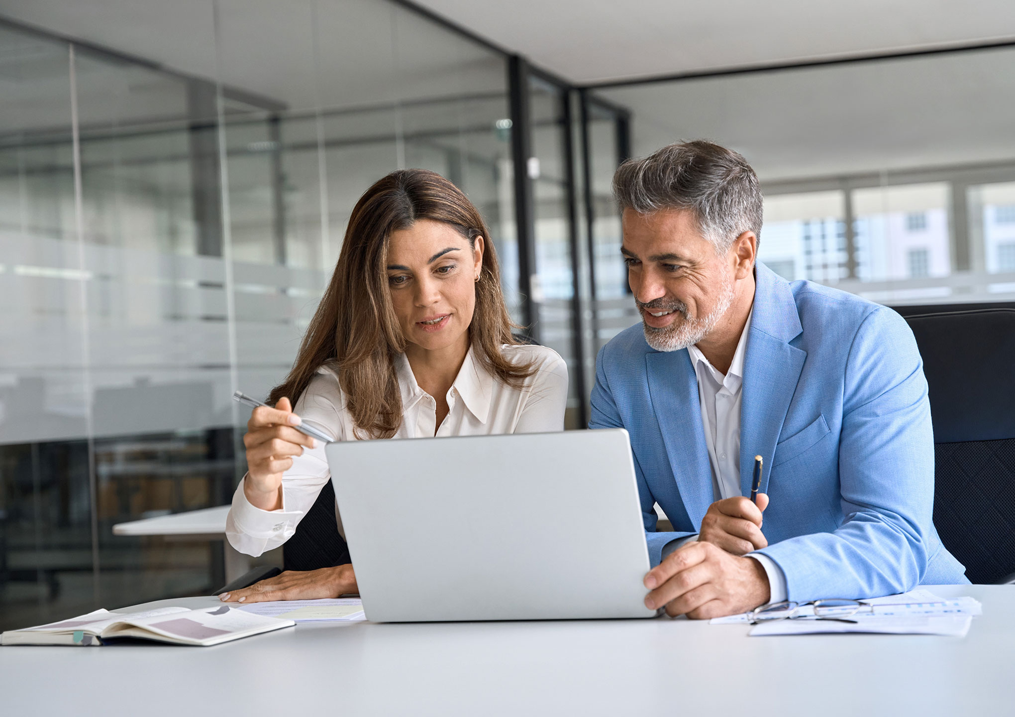 Two busy happy middle aged professional business man and woman executive leaders team using laptop working on computer at work desk having conversation on financial project at meeting in office.